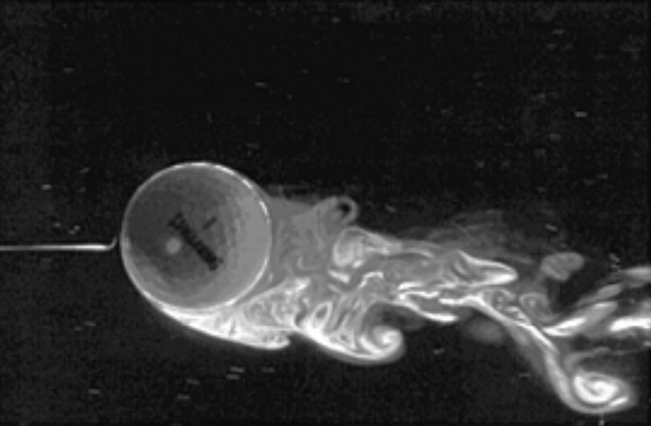Wind tunnel image of a spinning golf ball — flow deflected downward producing backspin lift; visible vortex wake behind the ball