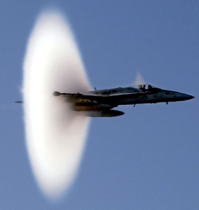 Photograph of an aircraft in transonic flight — water vapor condensation visible behind a mid-wing shock wave
